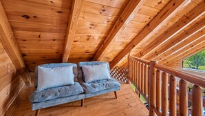 A wooden deck with a wooden railing, a blue sofa with pillows, and a view of greenery outside. - Douglas Lake Log Cabin | Game Room, Big Yard, Sleeps 6 (Sevierville)