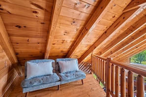 A wooden deck with a wooden railing, a blue sofa with pillows, and a view of greenery outside. - Refreshed 2BR Cabin w/ Game Room | Big Yard | Douglas Lake Area, Sevierville (Sevierville)