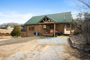 A log cabin with a green roof, a porch, and a gravel driveway. - Refreshed 2BR Cabin w/ Game Room | Big Yard | Douglas Lake Area, Sevierville (Sevierville)
