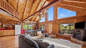 A spacious cabin interior with a high ceiling, wooden walls, a kitchen area, a living room with a sofa, and a fireplace. - Douglas Lake Log Cabin | Game Room, Big Yard, Sleeps 6 (Sevierville)
