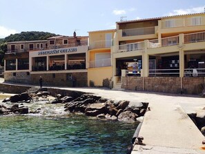 A waterfront building with a restaurant named 'RESTAURANT DES AMIS' and a stone wall with a small stream. - Campomoro - Beach apartment (Belvédère-Campomoro)