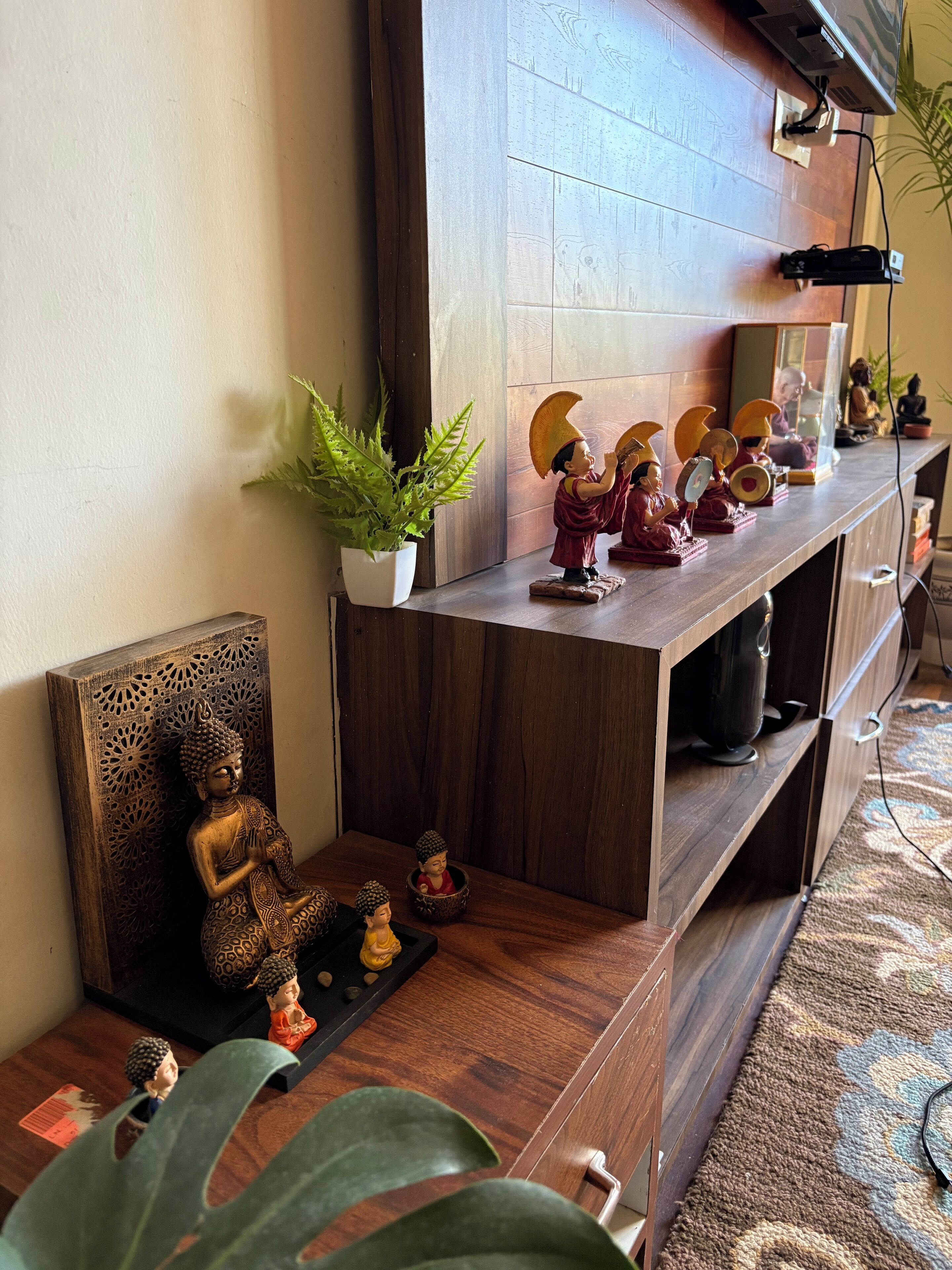 Una estantería de madera con adornos, una estatua de Buda y una planta en maceta.