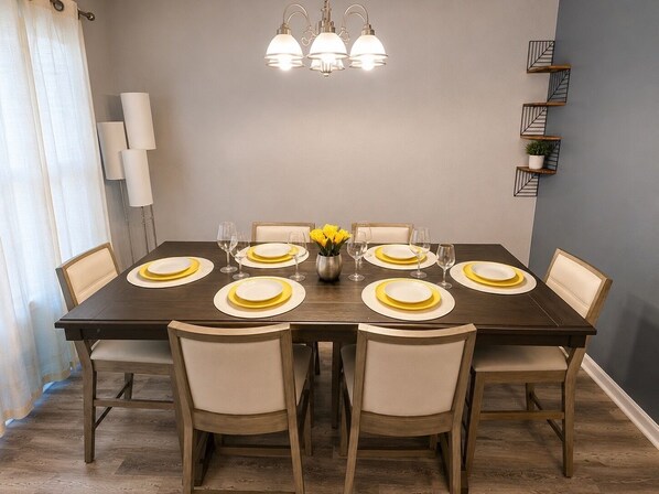 A dining room with a dark wooden table set for eight, surrounded by beige upholstered chairs.