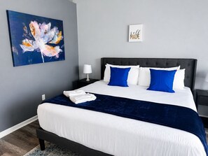 A neatly made bed with white and blue bedding, a dark headboard, and a wall-mounted painting.