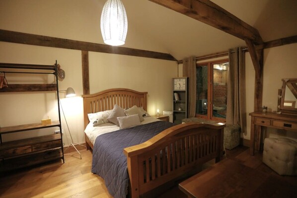 A bedroom with a wooden bed, a bedside table, a lamp, a shelf, and a window with curtains.