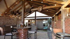 An outdoor patio area with brick walls, wooden beams, and a bar counter.