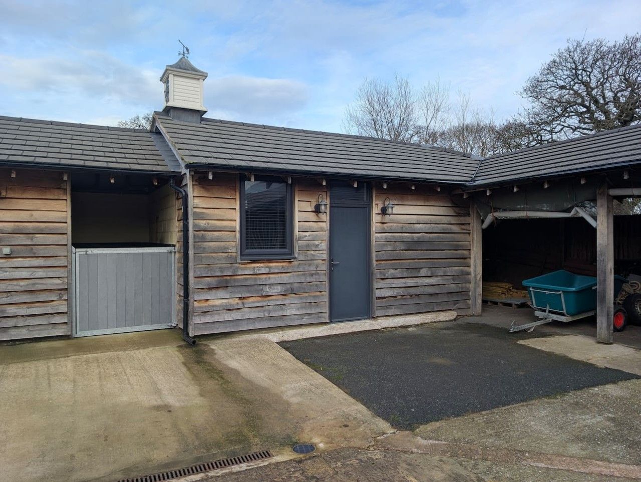 Une construction en bois comprenant un garage, un espace abrité et une allée en béton.