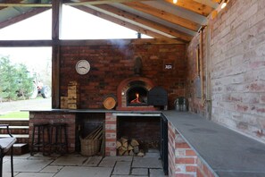 A brick-built outdoor kitchen with a wood-fired oven, a clock, and a rustic setting.