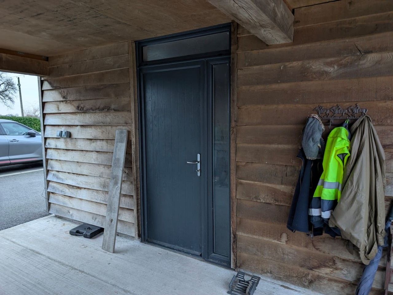 Une cabane en bois avec une porte sombre, une marche en béton et une boîte à outils en métal posée sur le sol.