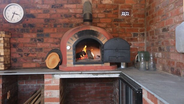 A brick oven pizza oven with a clock on the wall.