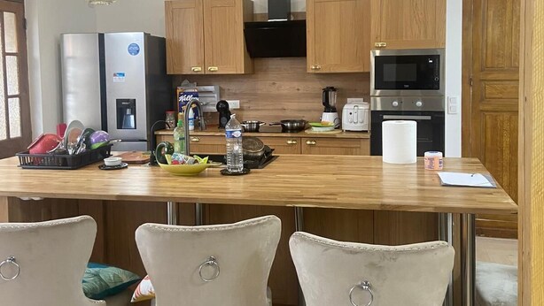 A kitchen with wooden cabinets, a stainless steel refrigerator, a microwave, and a wooden dining table with four chairs. - Getaway & wellness Charming house (Ravenel)