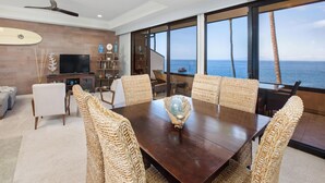 Uma sala de estar ampla com uma grande mesa de jantar, assentos confortáveis, televisão e vista para o oceano.