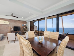 A spacious living room with a large dining table, comfortable seating, a television, and a view of the ocean. - Makena Surf F207 Beachfront Resort (Wailea)