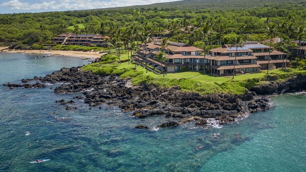 Resort costeiro com vários edifícios, litoral rochoso e águas azul-claras.