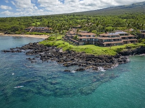 A coastal resort with multiple buildings, a rocky shoreline, and clear blue waters. - Makena Surf F207 Beachfront Resort (Wailea)