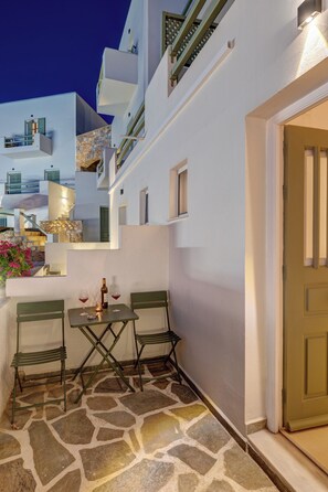 A stone-floored outdoor seating area with a table and chairs, a door, and a white building with balconies.