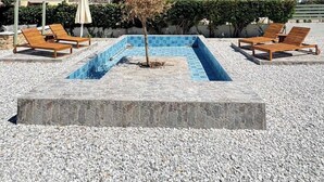 A swimming pool with lounge chairs and umbrellas, surrounded by pebbles and a mountain in the background.