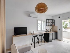 A modern kitchen with a TV, bar stools, a hanging light, and a view of the outside.