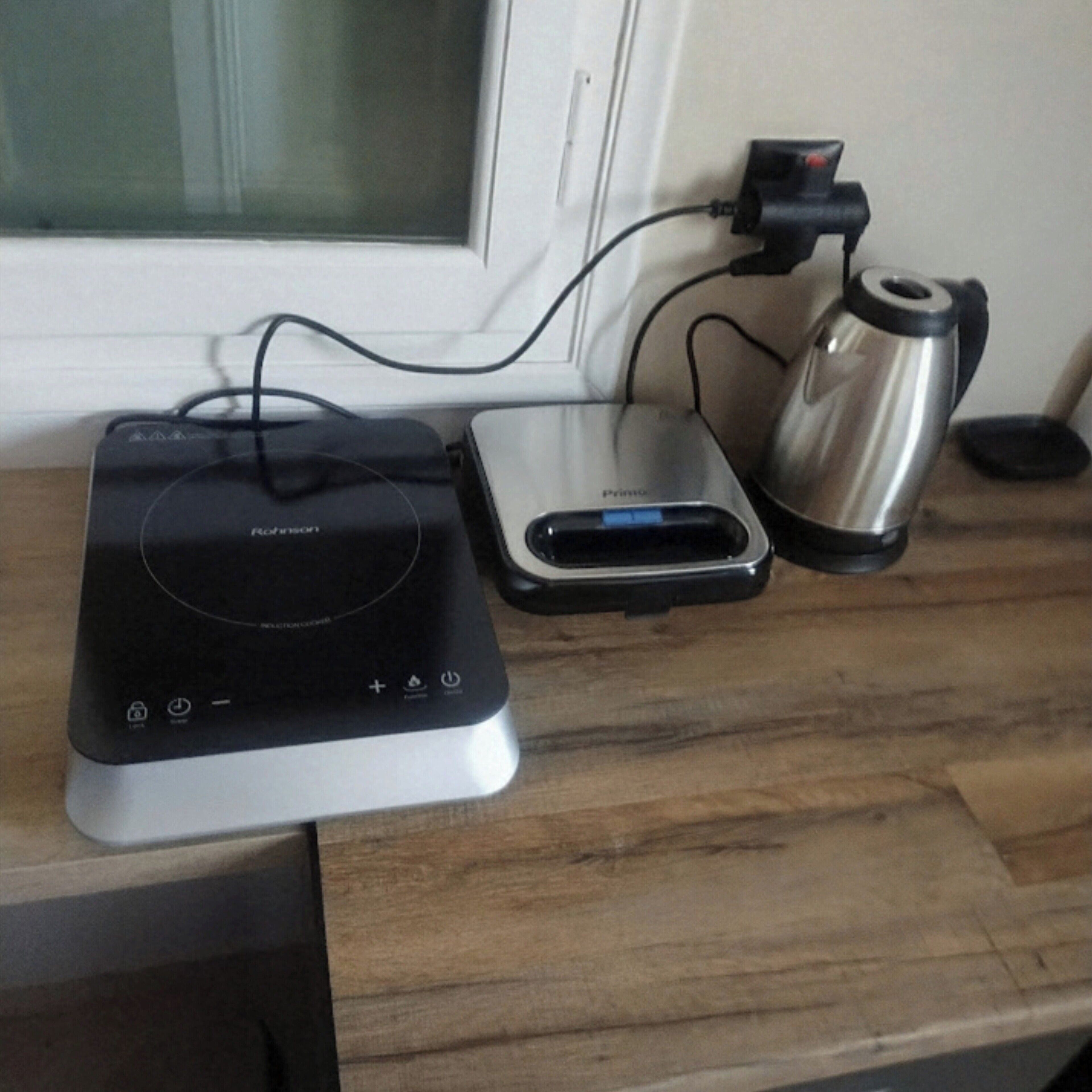 Une cuisine équipée d’un cuiseur à riz, d’une machine à café et d’un autre cuiseur à riz, le tout posé sur un plan de travail en bois.