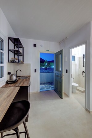 A modern kitchen with a wooden countertop, a black chair, and a view of a garden through an open door.