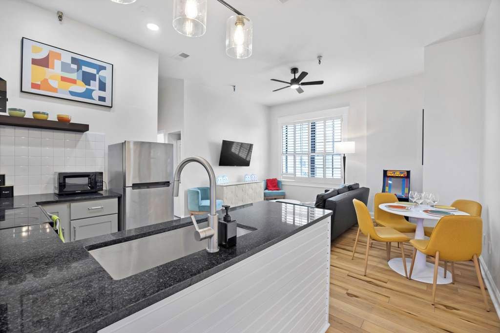 A modern kitchen with a granite countertop, stainless steel appliances, and a dining area with yellow chairs and a white table.