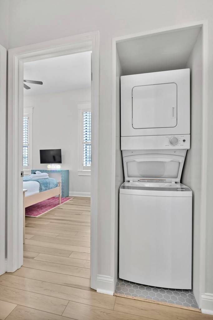 Ein gemütlicher Raum mit integrierter Waschmaschine und Trockner, einem Bett mit blauer Kopfteil, einem Fernseher auf einem Schrank und einem Fenster mit Jalousien.