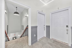 Un couloir avec deux portes blanches, un escalier et un luminaire suspendu.
