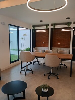 Una sala de reuniones moderna con una larga mesa, cuatro sillas, una mesita con una planta y una pared de ladrillo.