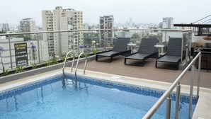 A rooftop pool with lounge chairs, a view of the cityscape, and a sign advertising a visit to a pilot. - Stylish Studio in Bohemian Barranco · Work-Ready · Steps from Miraflores (Barranco)