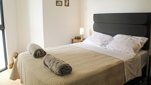 A neatly made bed with a patterned bedspread, a rolled towel, and a bedside lamp. - Stylish Studio in Bohemian Barranco · Work-Ready · Steps from Miraflores (Barranco)