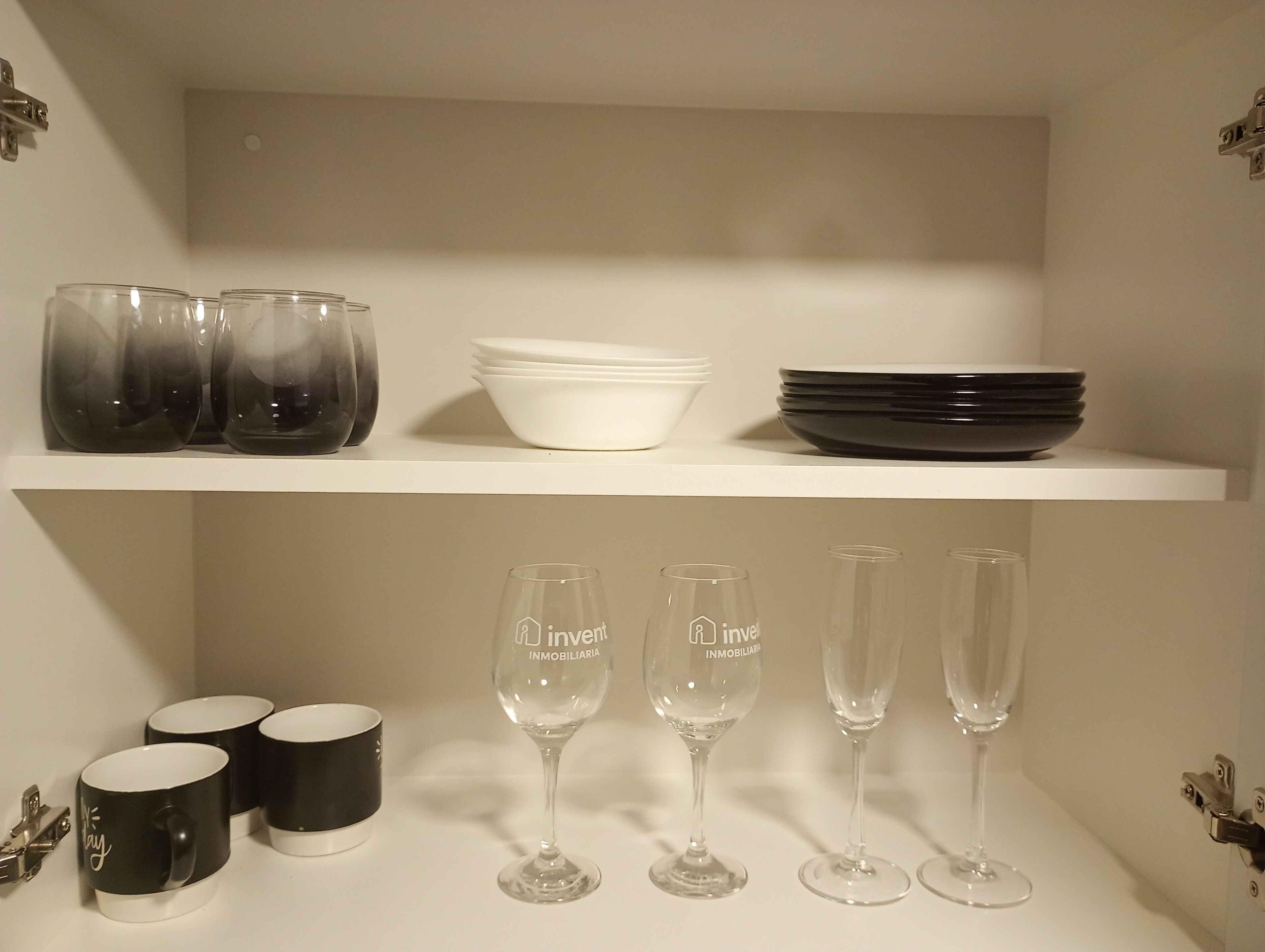 A shelf with clear glassware, black and white mugs, and stacked plates.