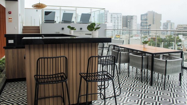 A modern outdoor kitchen with a wooden island, black metal chairs, and a patterned floor. - Stylish Studio in Bohemian Barranco · Work-Ready · Steps from Miraflores (Barranco)