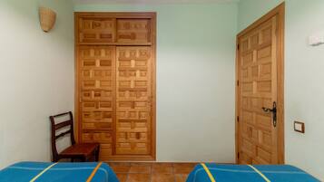 Une chambre avec deux lits, une armoire en bois, une chaise et un luminaire fixé au mur.