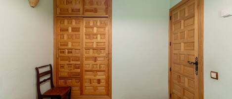 A room with two beds, a wooden wardrobe, a chair, and a wall-mounted light fixture.