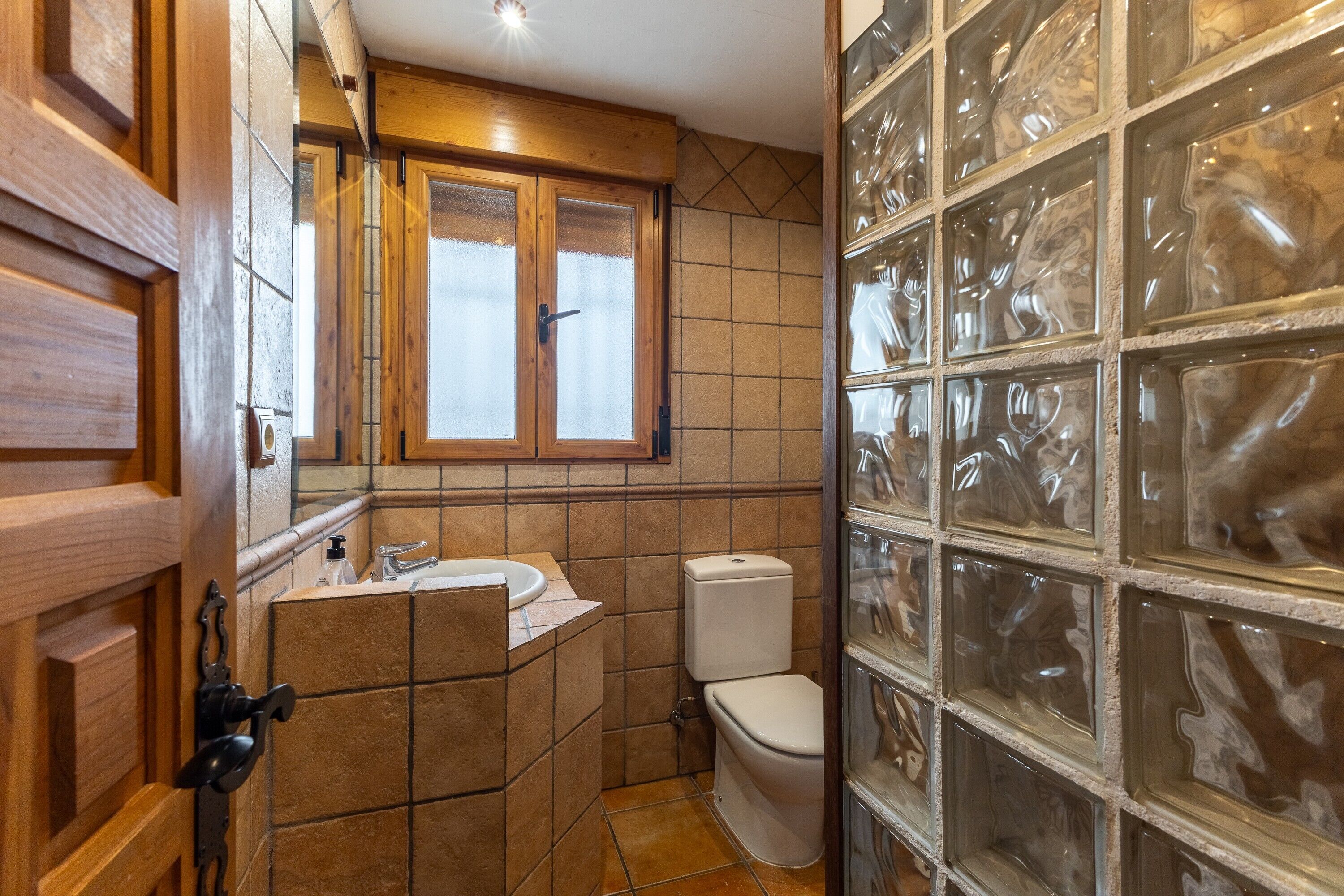 A bathroom with a wooden vanity, a toilet, and a glass block wall.