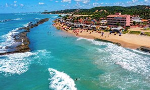 Um hotel à beira-mar, com praia, vista para o oceano e um trecho de costa rochosa.