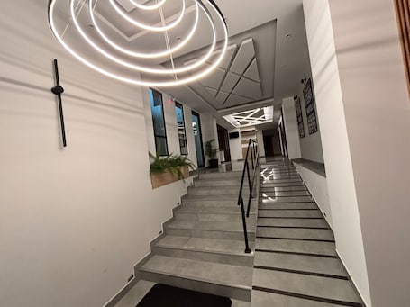 A modern staircase with a geometric light fixture, a handrail, and a potted plant on the left.. Rio Skyline : Luxury + WiFi 850 Mbps + Parking