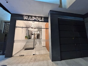 Une entrée moderne avec une porte en verre, un escalier menant à l’intérieur et une enseigne sur laquelle on peut lire « NAPOLI ».