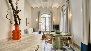 Een moderne kamer met een marmeren vloer, een ronde tafel met stoelen, een bank met kussens, een decoratieve oranje vaas en een raam met gordijnen.