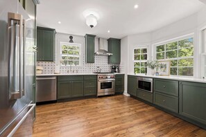 Una cocina con gabinetes verdes, un refrigerador de acero inoxidable, un horno empotrado y una ventana con vistas a árboles.