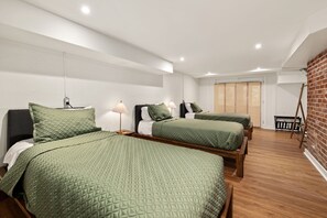 Una habitación con dos camas, piso de madera, pared de ladrillo y una ventana con persianas.
