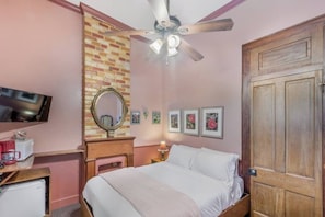 Quarto com cama, ventoinha no teto, televisão, espelho, lareira e quadros nas paredes.