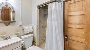 A bathroom with a toilet, sink, mirror, shower curtain, and wooden door. - French Quarter Jazz Hideaway and Courtyard (New Orleans)
