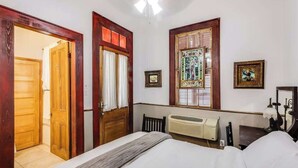 A bedroom with a bed, a radiator, a wooden door, and a window with a stained glass design. - French Quarter Jazz Hideaway and Courtyard (New Orleans)