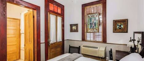 A bedroom with a bed, a radiator, a wooden door, and a window with a stained glass design.