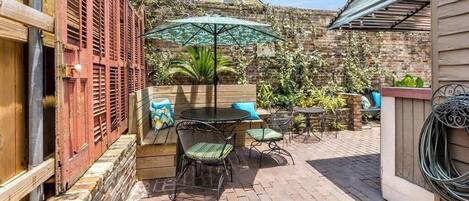 A patio area with a table and chairs, a wooden bench, and a brick wall.