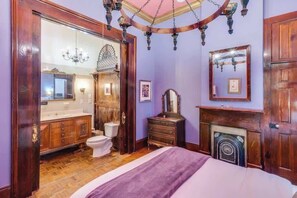 Quarto com piso de madeira, cama, cômoda, espelho e lareira.