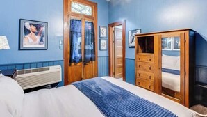 Ein Schlafzimmer mit Bett, einem Holzschrank, einem Fenster mit Vorhängen und einem Wandheizkörper.