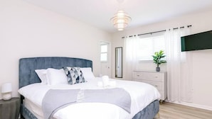 Een moderne slaapkamer met een groot bed, nachtkastjes, een dressoir, een televisie en een raam met gordijnen.