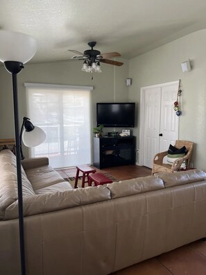 Ein Wohnzimmer mit einer Couch, einem Fernseher, einem Deckenventilator und einer Tür.